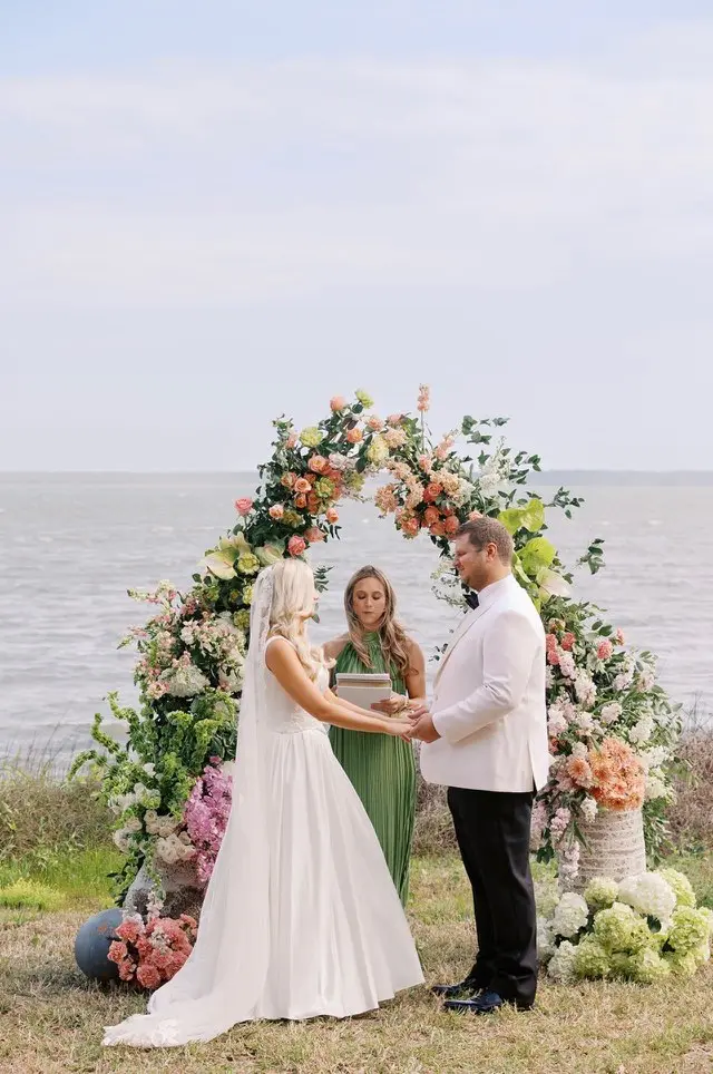 A ceremony beneath a floral arch at the water.