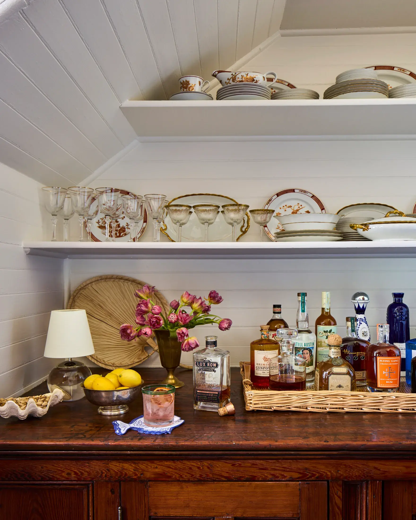 The pantry under the eaves, china on open shelves above a wooden bar.