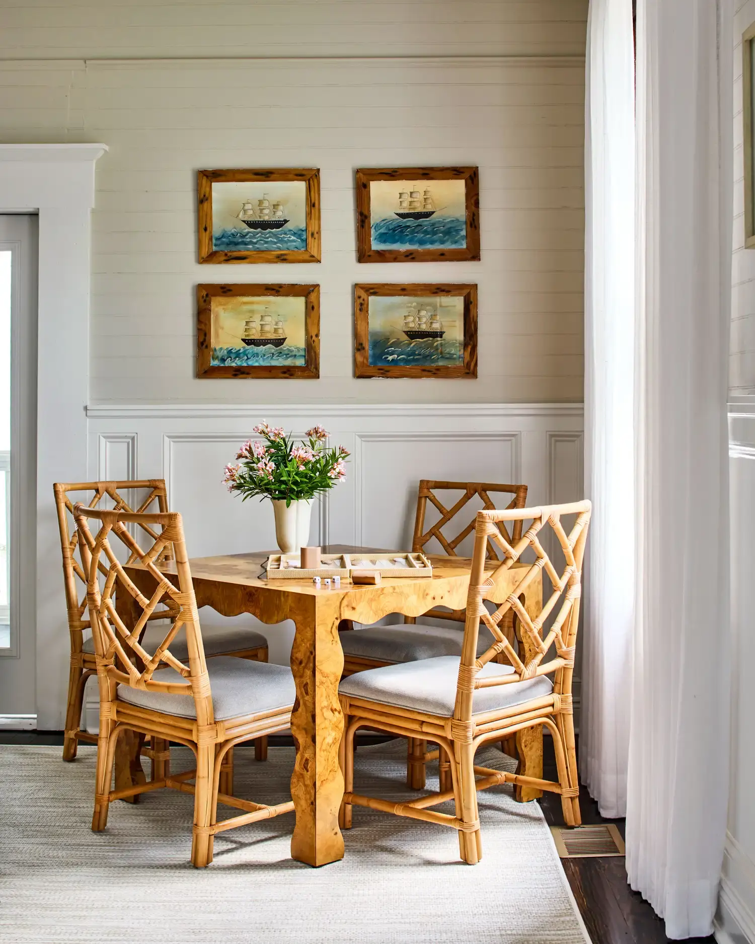 A bamboo table and chairs in the game room at 11 Mile, beneath four small ship paintings.