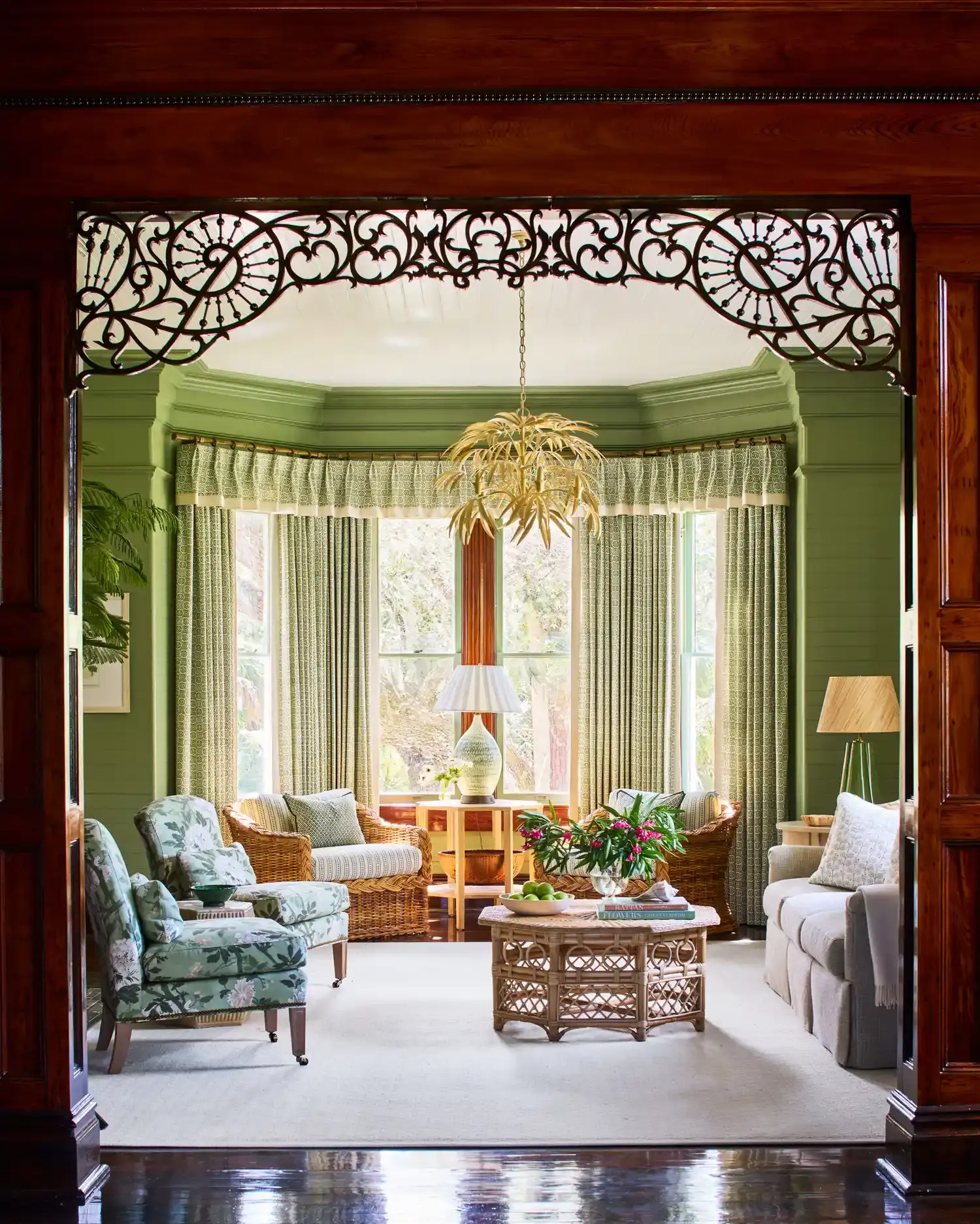 A sage-green sitting room seen through a carved fretwork arch, with a bay window onto the water.