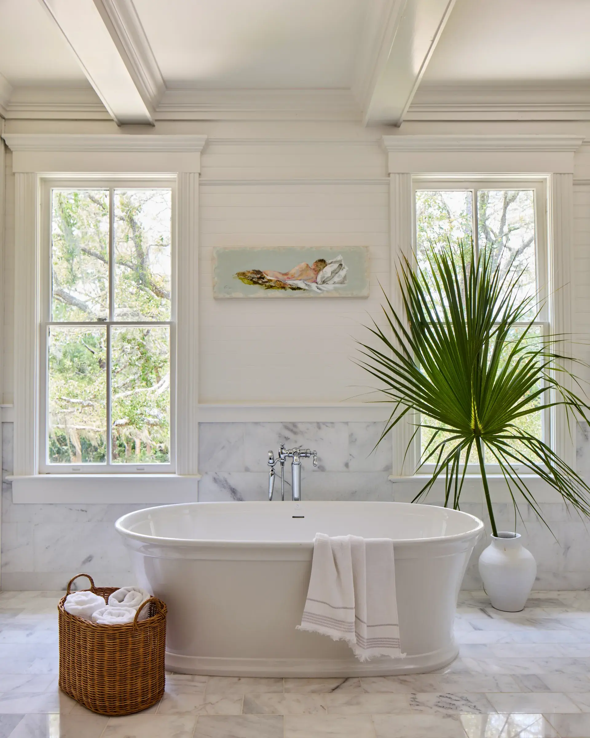 A freestanding tub against marble tile under a coffered ceiling.