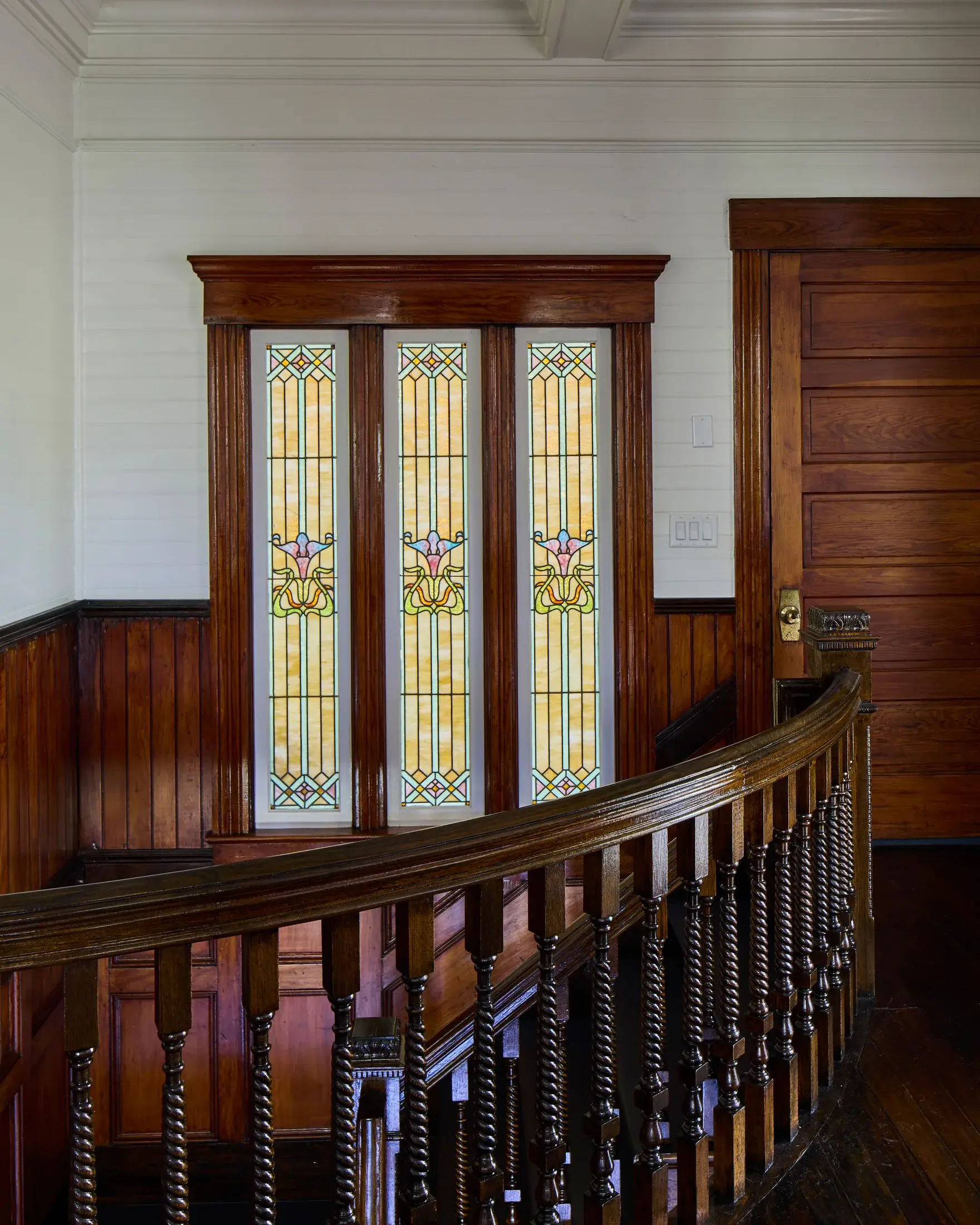 Three Art Nouveau stained-glass panels above the balusters of the stair landing.